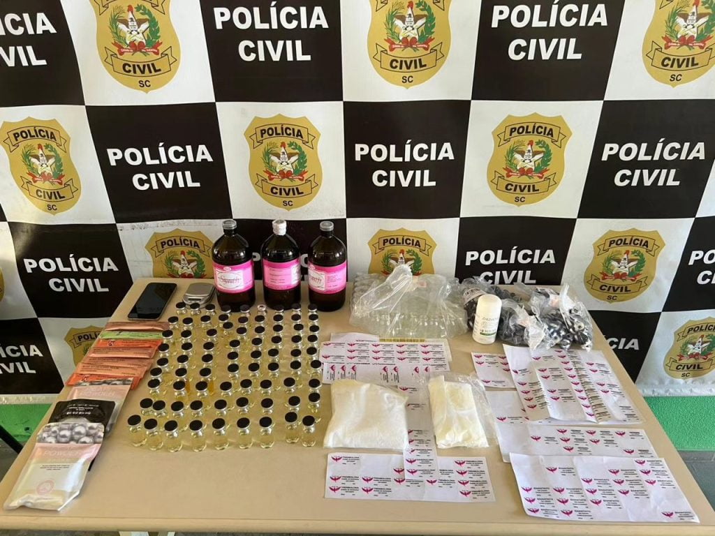 Imagem mostra mesa com anabolizantes e bandeira da polícia civil