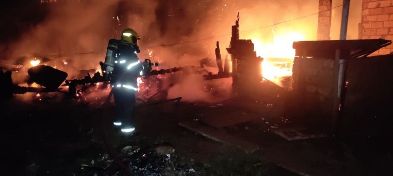 Foto mostra escombros em chamas e bombeiros trabalhando para conter incêndio
